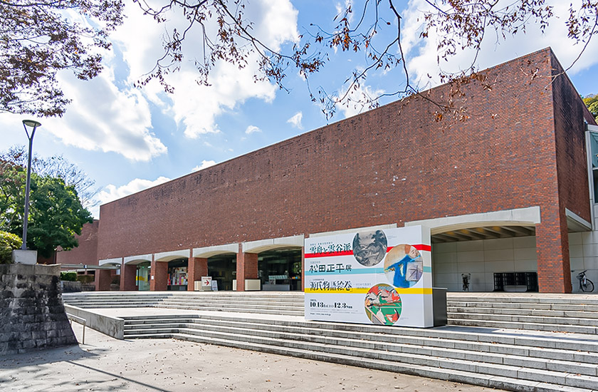 画像：山口県立美術館。レンガタイルで覆われた外観で玄関前に大きな展覧会の看板が掲示されている